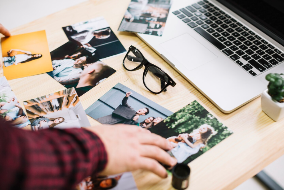 Photos on a desk beside a laptop, representing the need to back up digital and physical memories.