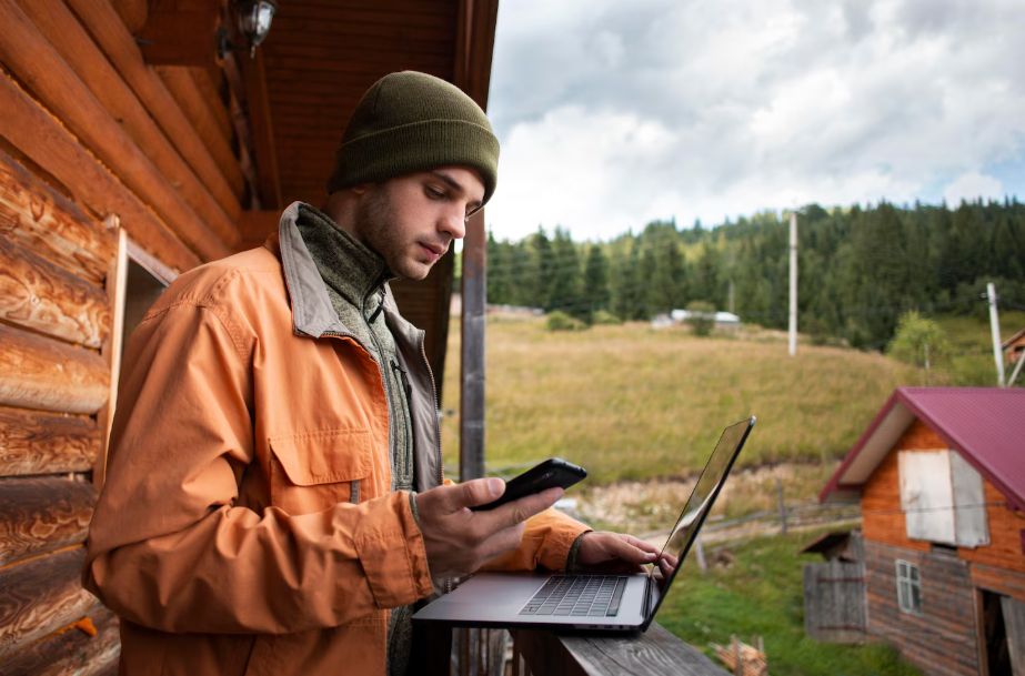 Man in a rural community using laptop and smartphone with satellite internet connectivity