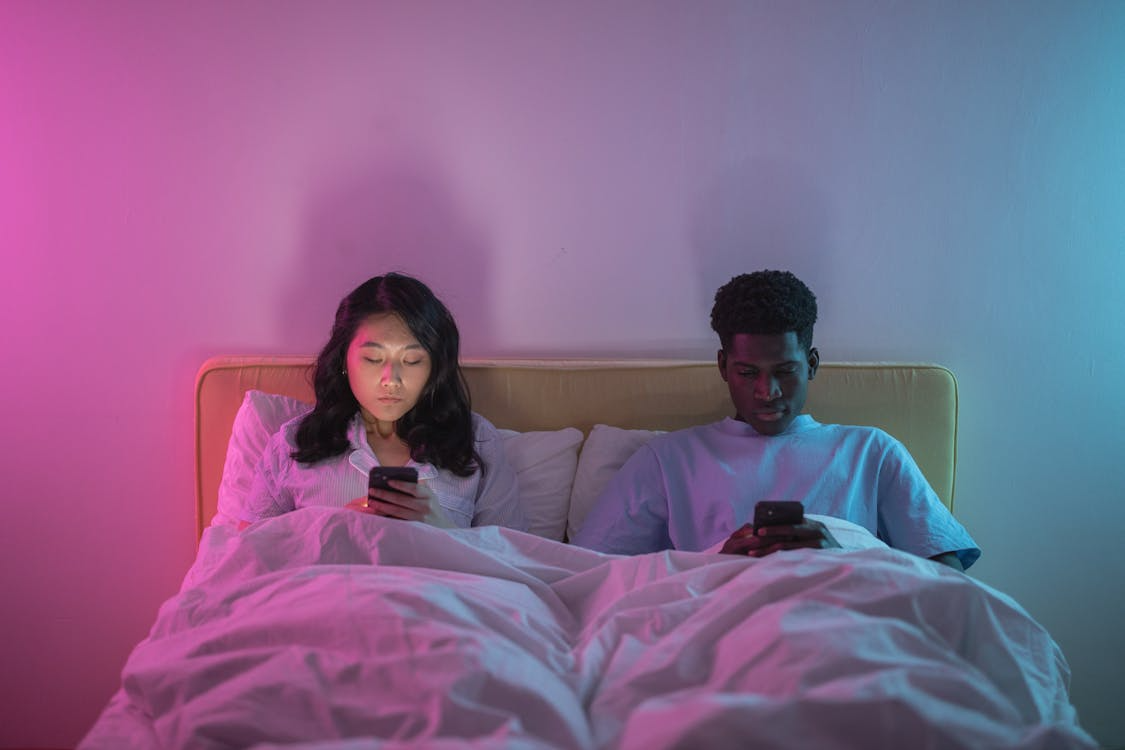 Couple lying in bed using smartphones instead of talking, illustrating the effects of texting on relationships