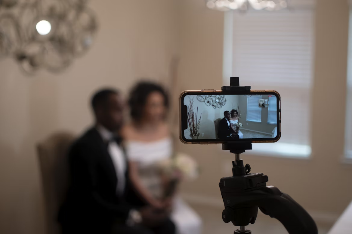 The bride and groom are livestreaming their wedding ceremony through a smartphone on a tripod.